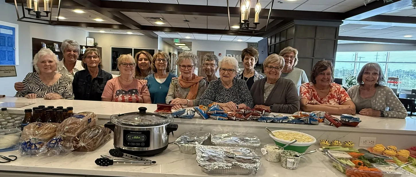 A homemakers group gathered behind a counter of prepared dishes in the House kitchen.