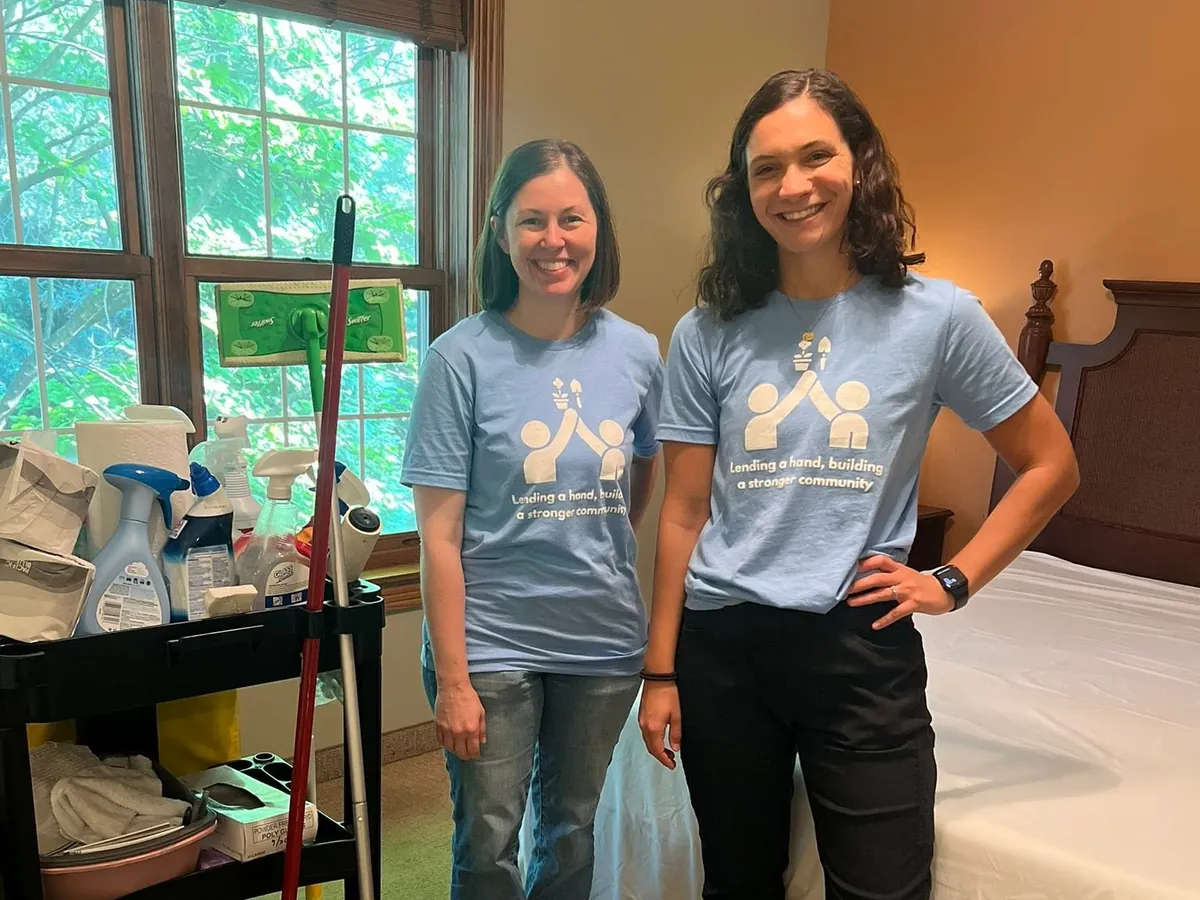 Two volunteers beside a cleaning cart in a guest room.