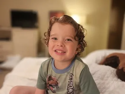 A smiling young child sitting on a bed.