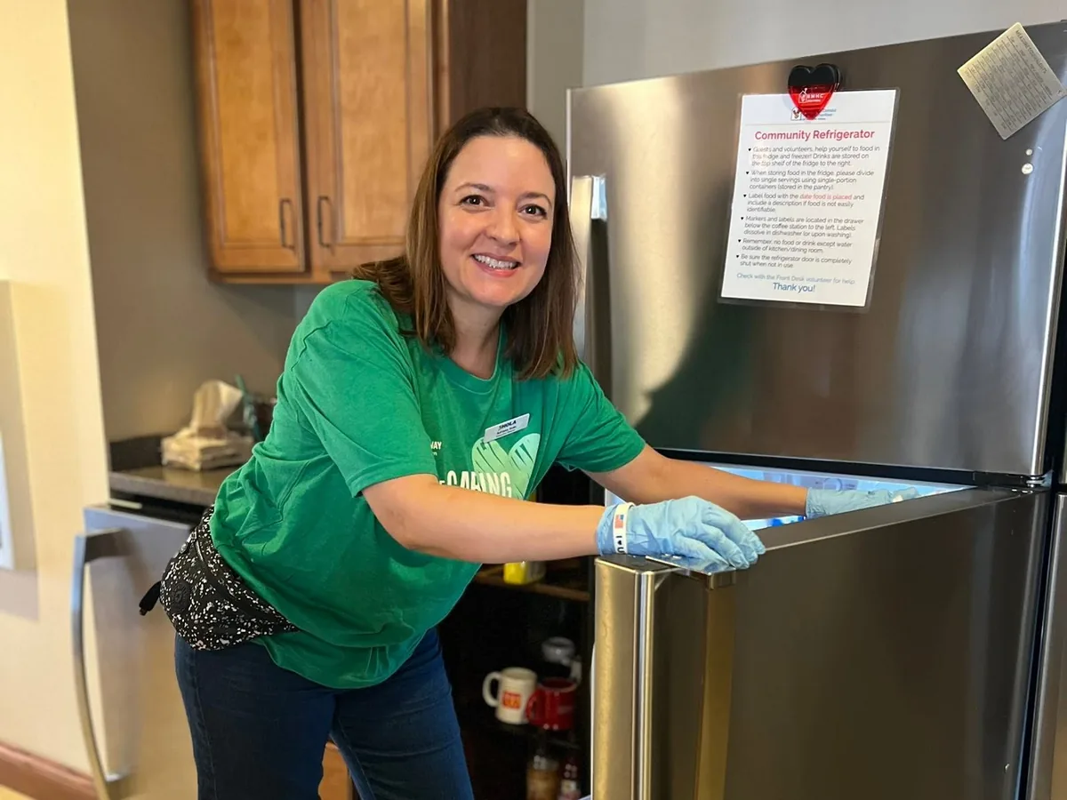 A volunteer in a green shirt cleaning a refrigerator at the House.
