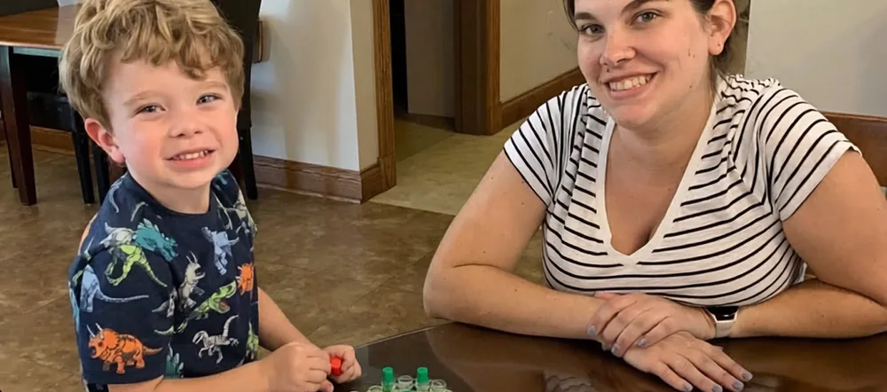 A mother and her young son smiling over a board game at the House.