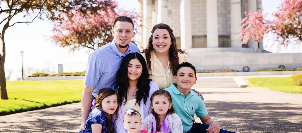 A smiling family of seven sitting together outdoors in spring.