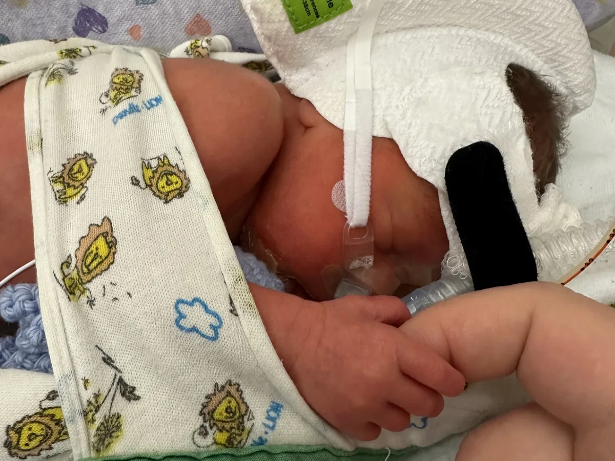 A newborn in the NICU holding a parent’s finger.