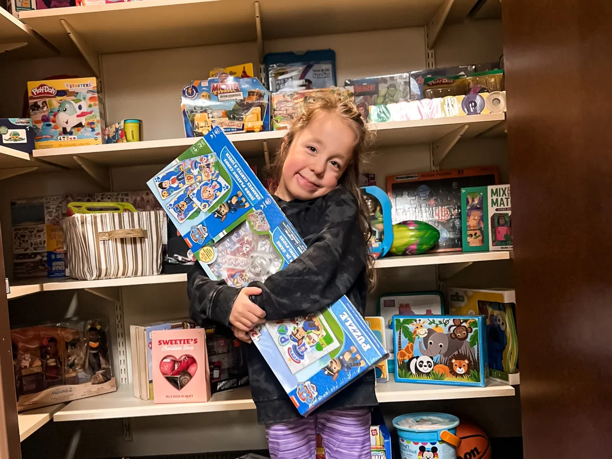 A young girl hugging a donated puzzle in the House toy closet.