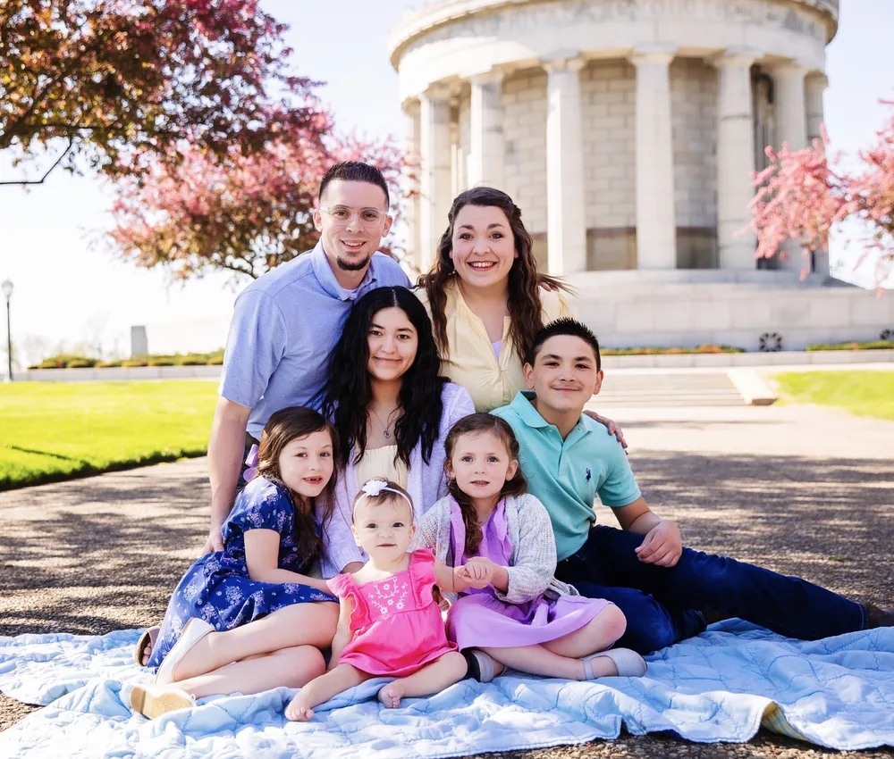 A smiling family of seven sitting together outdoors in spring.
