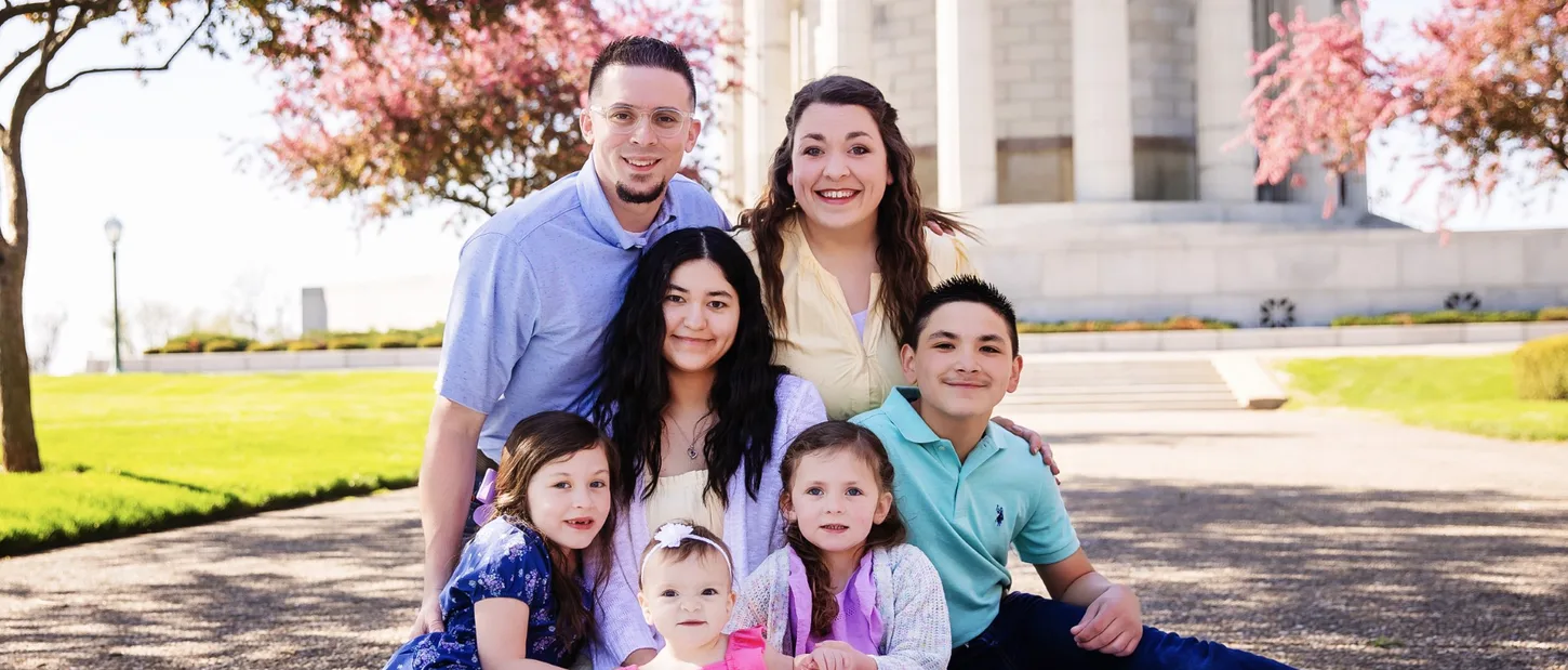 A smiling family of seven sitting together outdoors in spring.