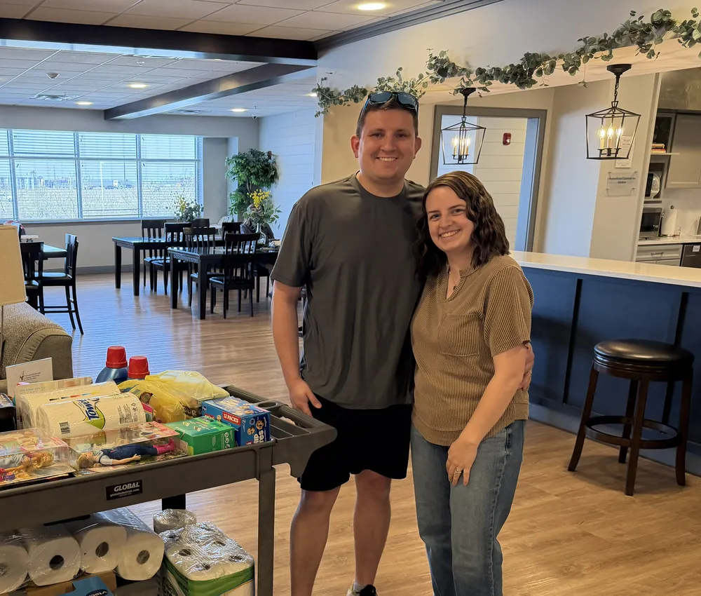 Two supporters stand beside a cart of donated supplies inside a Ronald McDonald House.