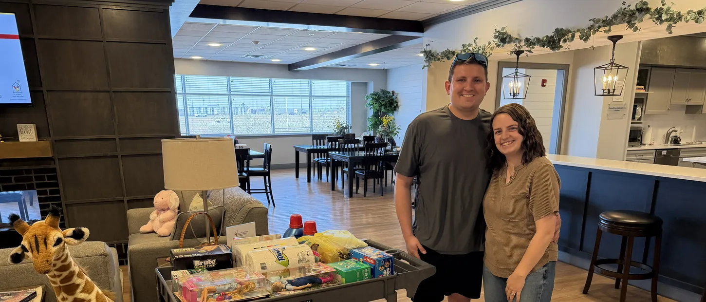 Two supporters stand beside a cart of donated supplies inside a Ronald McDonald House.
